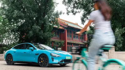 The new Xiaomi Electric Vehicle SU7 in front of a skyscraper formed out of a pair of conjoined towers.